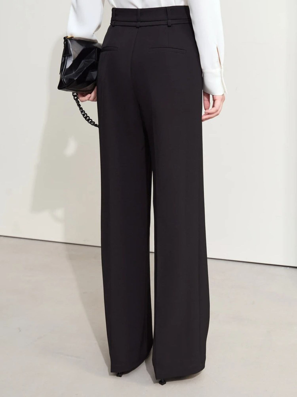 Side-back angle of black trousers with soft drape and ankle-length hem