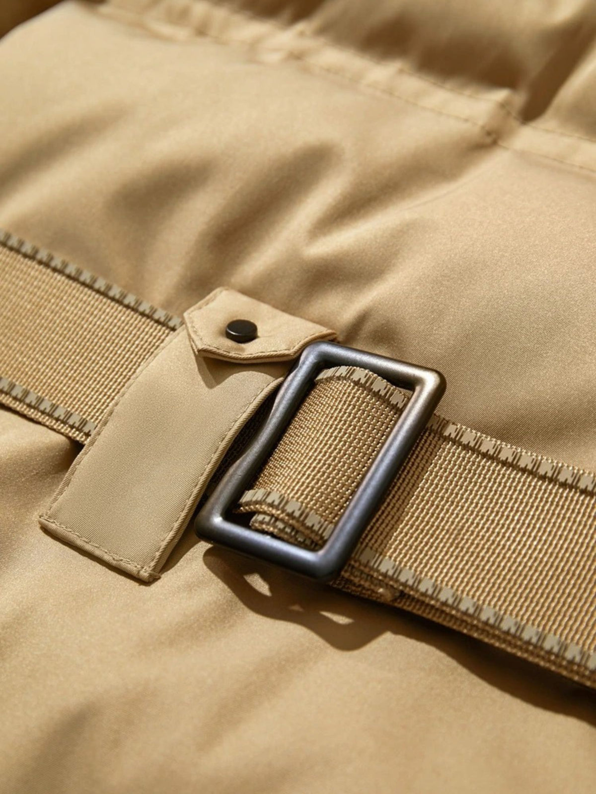 Close-up of belted waist on camel coat with silver buckle and stitching