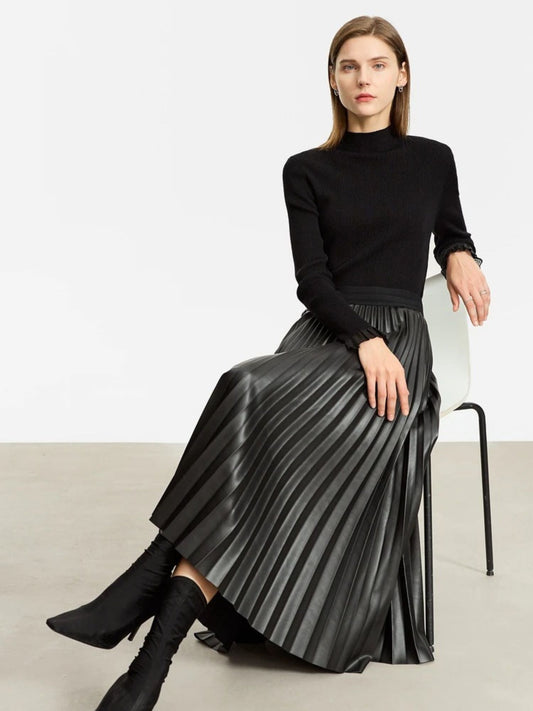 Model seated in black pleated faux leather midi skirt with ribbed black sweater and boots