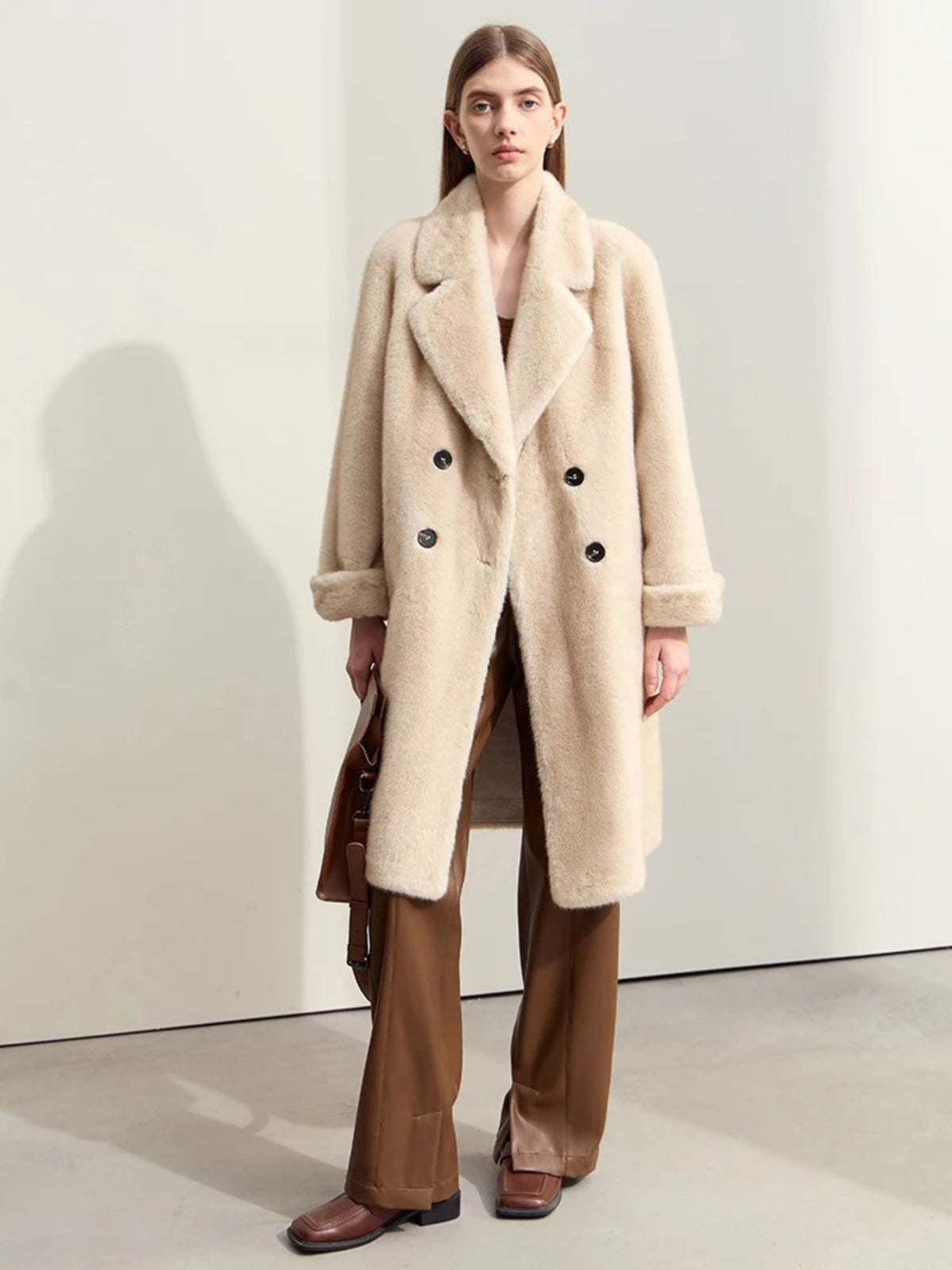 A female model wearing a beige faux fur double-breasted winter coat with a turn-down collar and raglan sleeves.