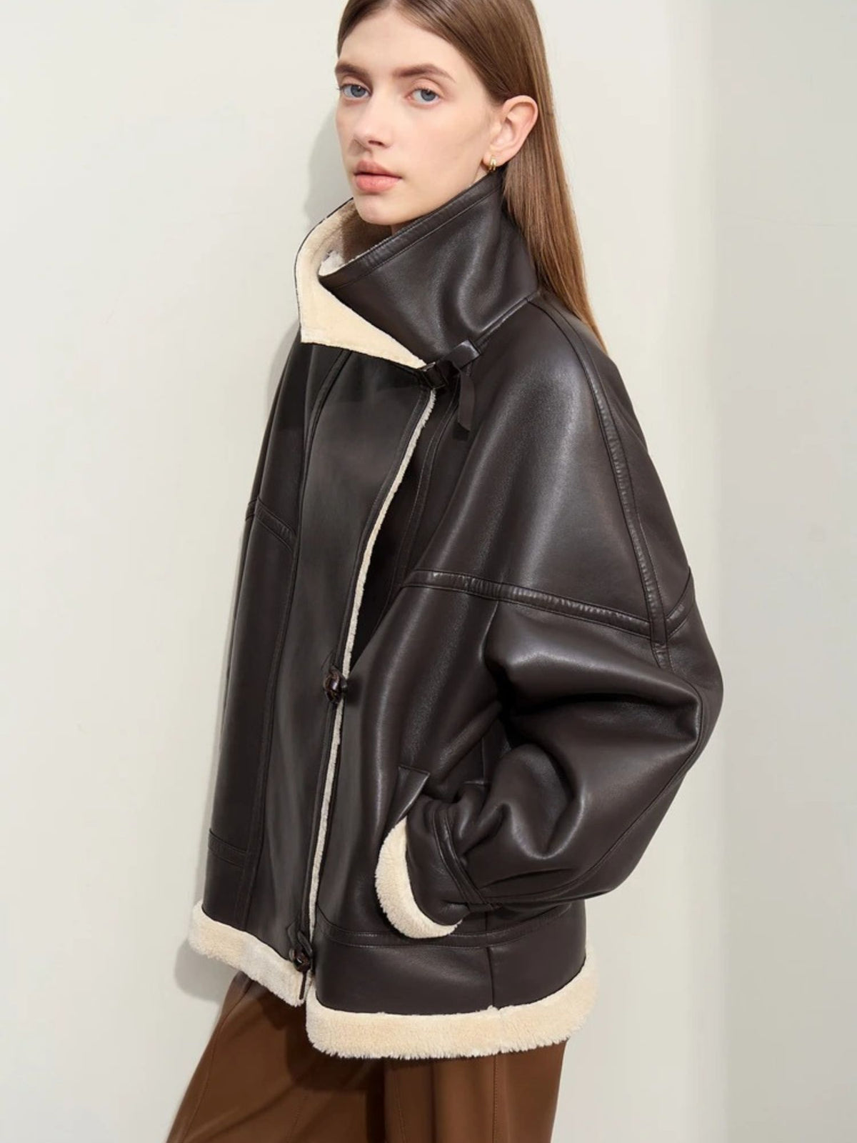 Angled side view of black aviator jacket with shearling trim, worn over brown trousers