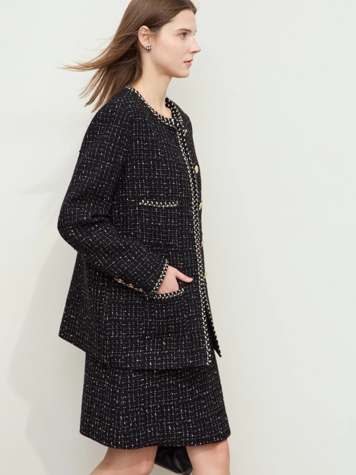 Side profile of black tweed jacket with structured shoulders and straight hem