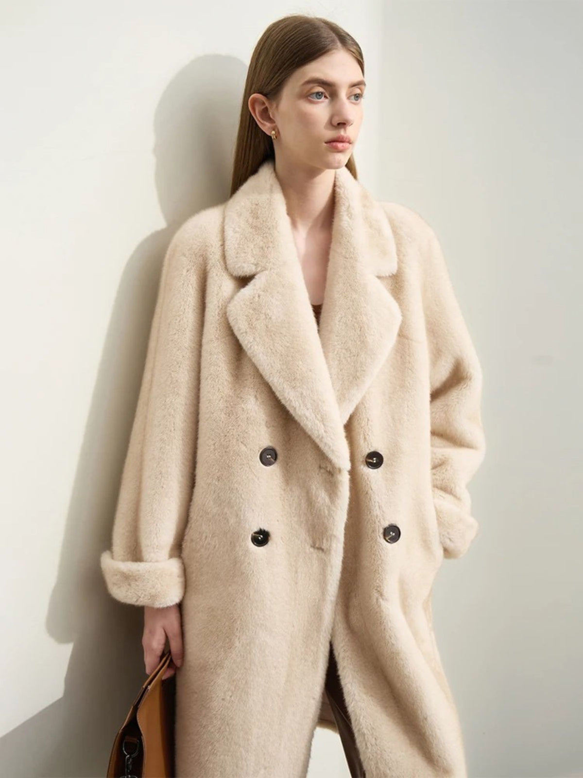 A female model wearing a beige faux fur double-breasted winter coat with a turn-down collar and raglan sleeves.