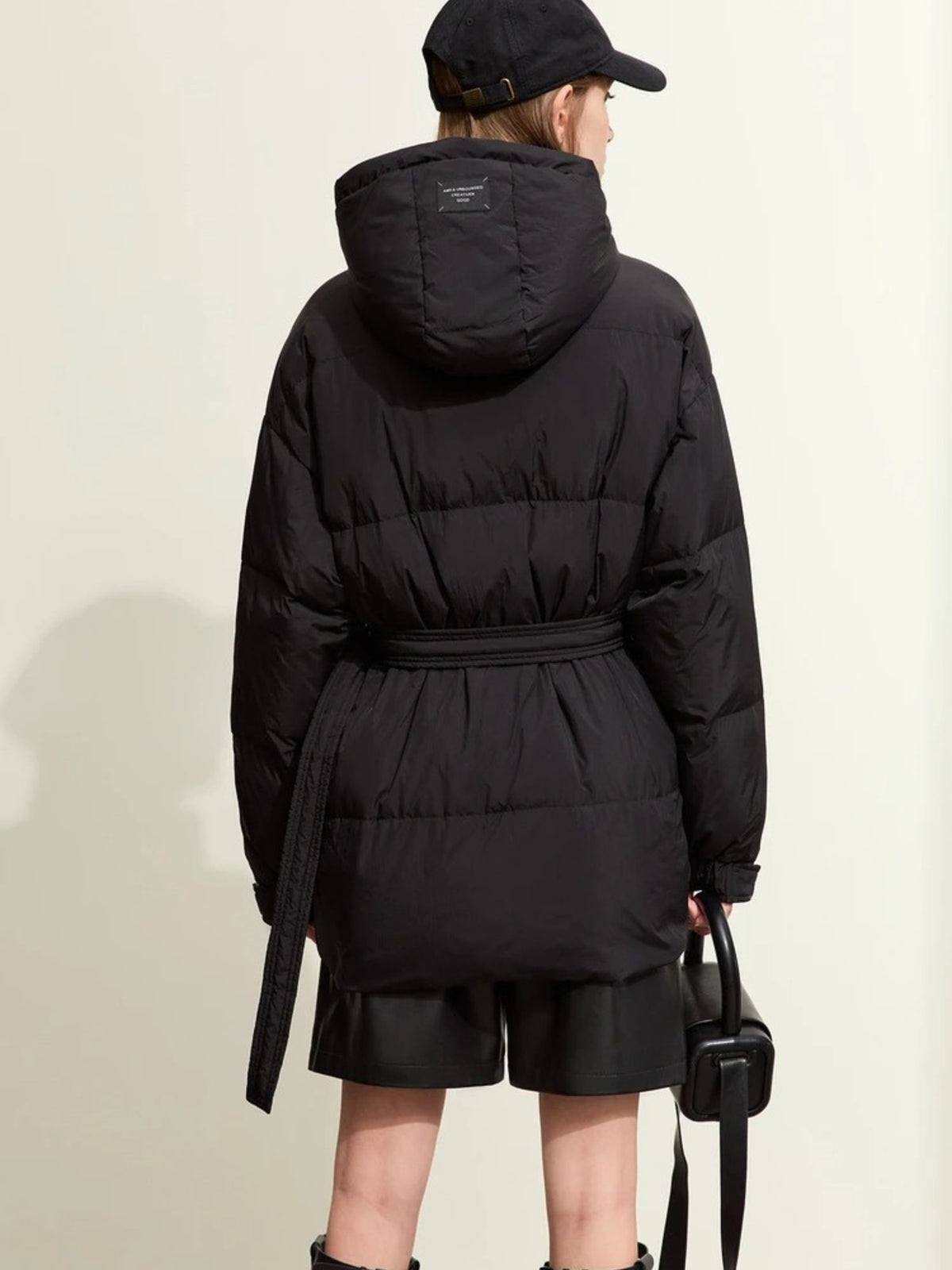 Back view of short black puffer jacket with belted waist and hood detail