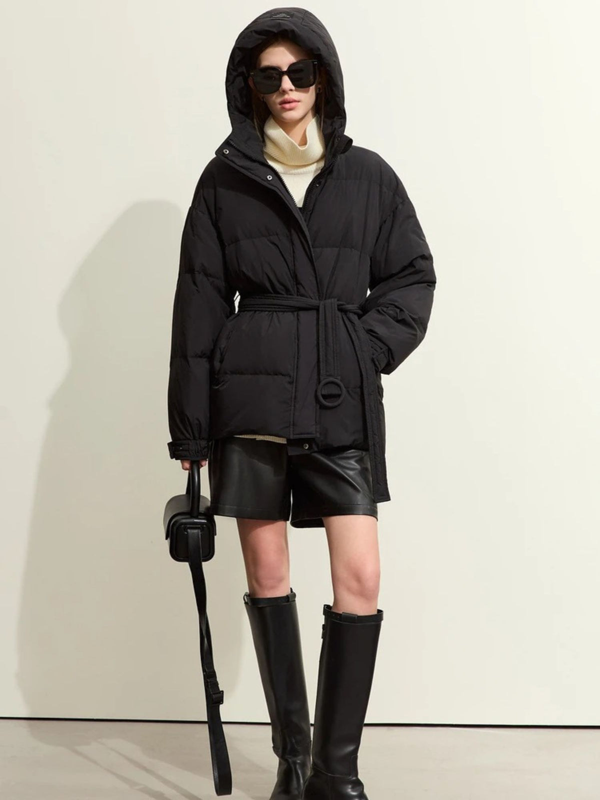 Black hooded puffer jacket with belted waist, styled with tall black boots