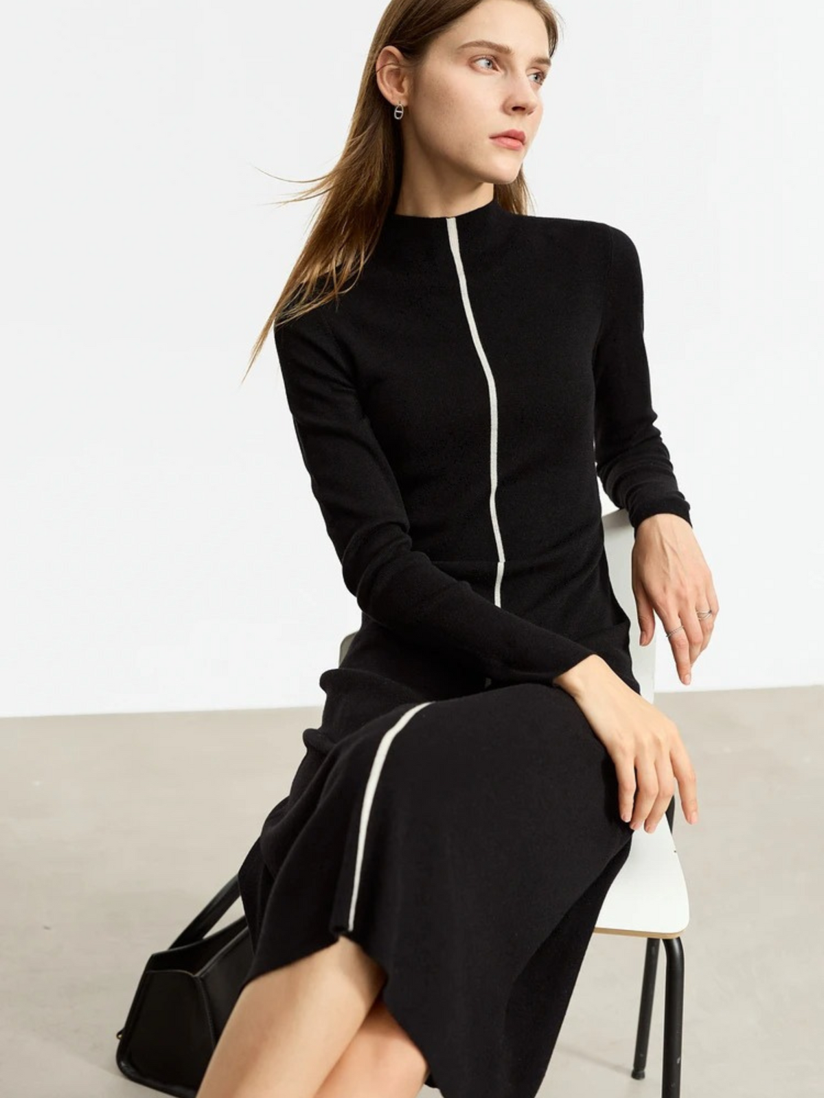 Black knit dress with front zipper, worn seated and styled with crossbody bag