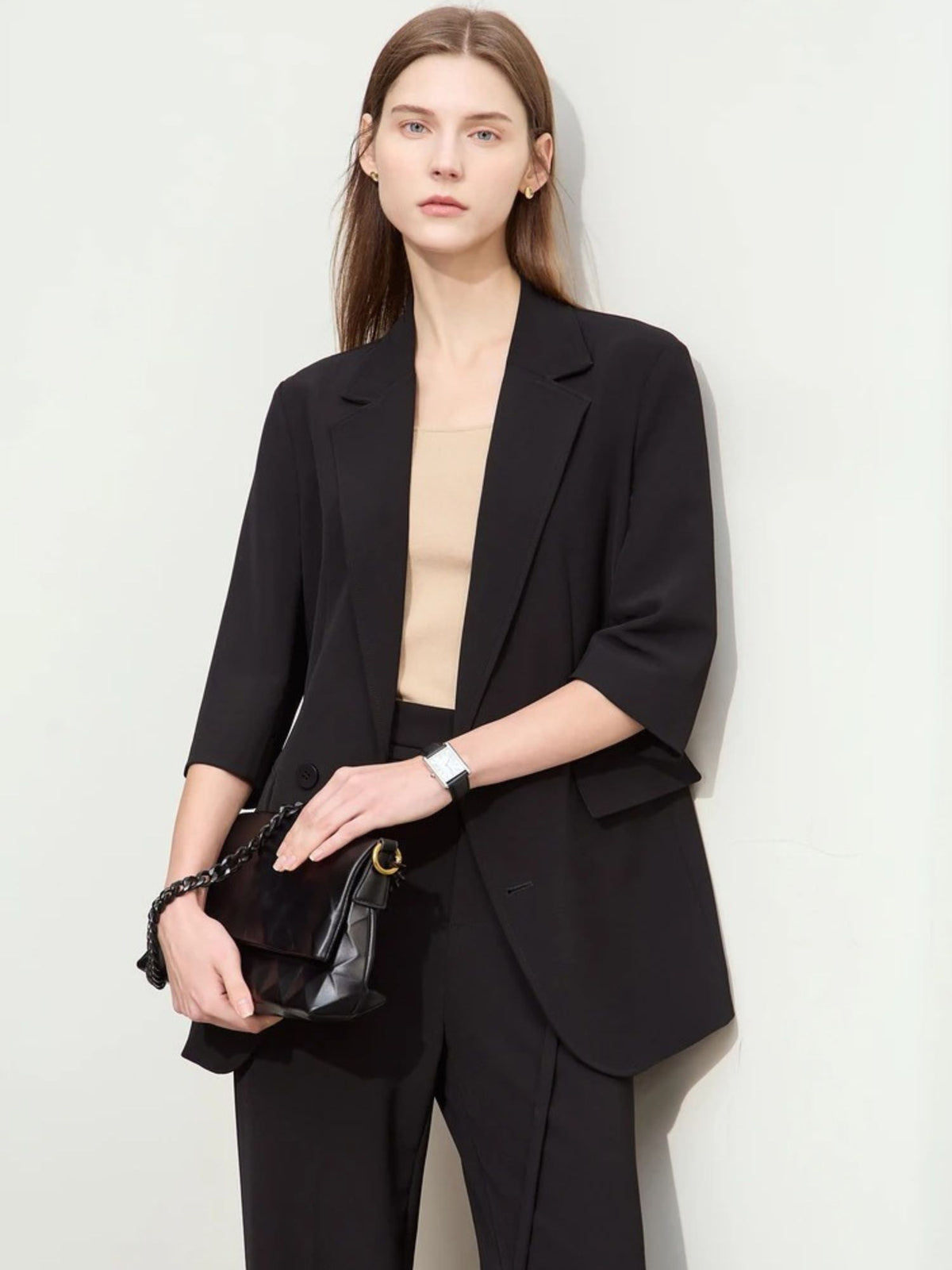Model holding clutch bag wearing relaxed black blazer and tailored trousers