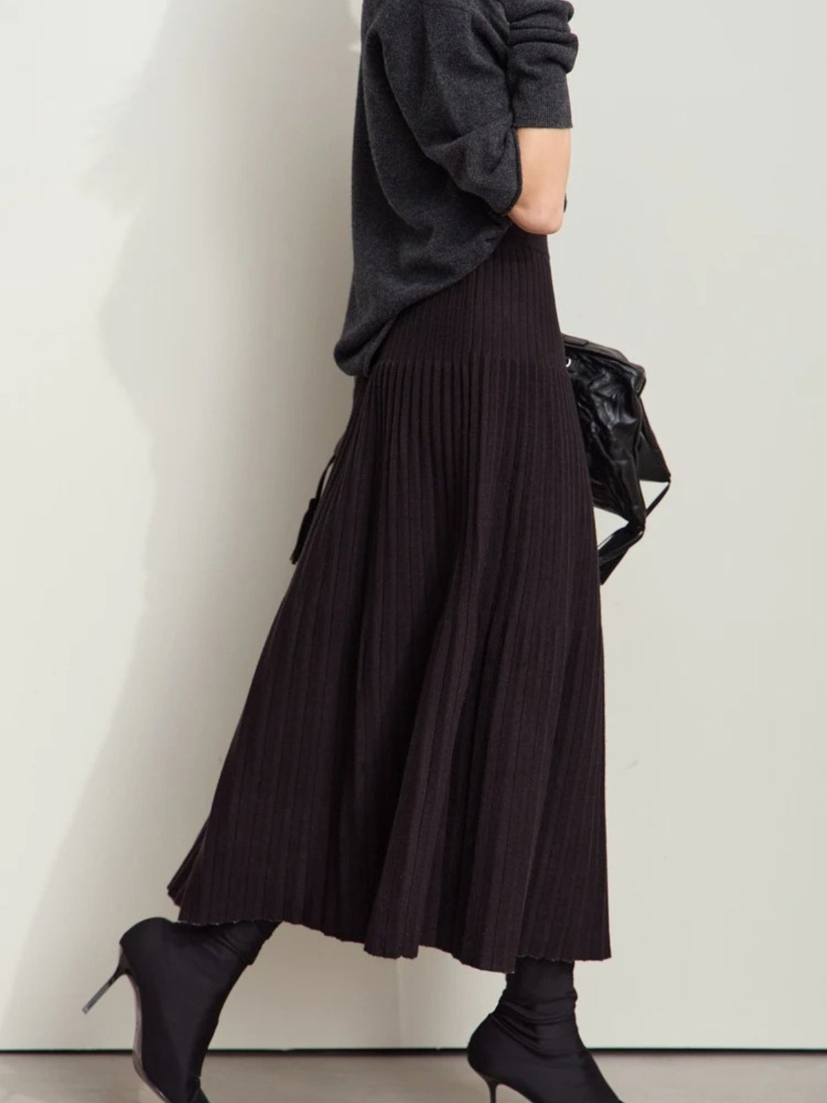 Side view of black and beige pleated skirt styled with long-sleeve knit top