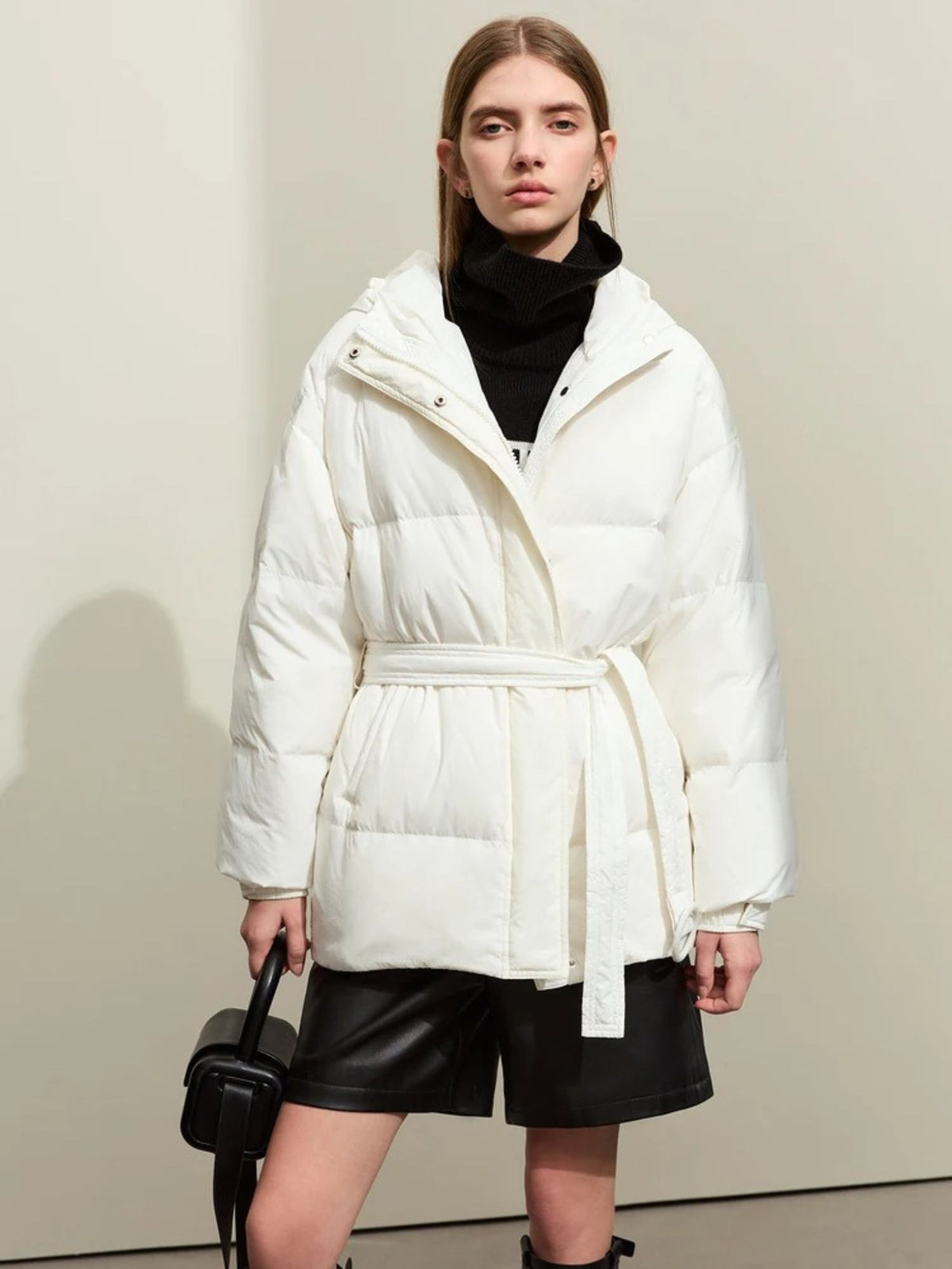 Front view of white belted puffer jacket with hood, styled with leather shorts