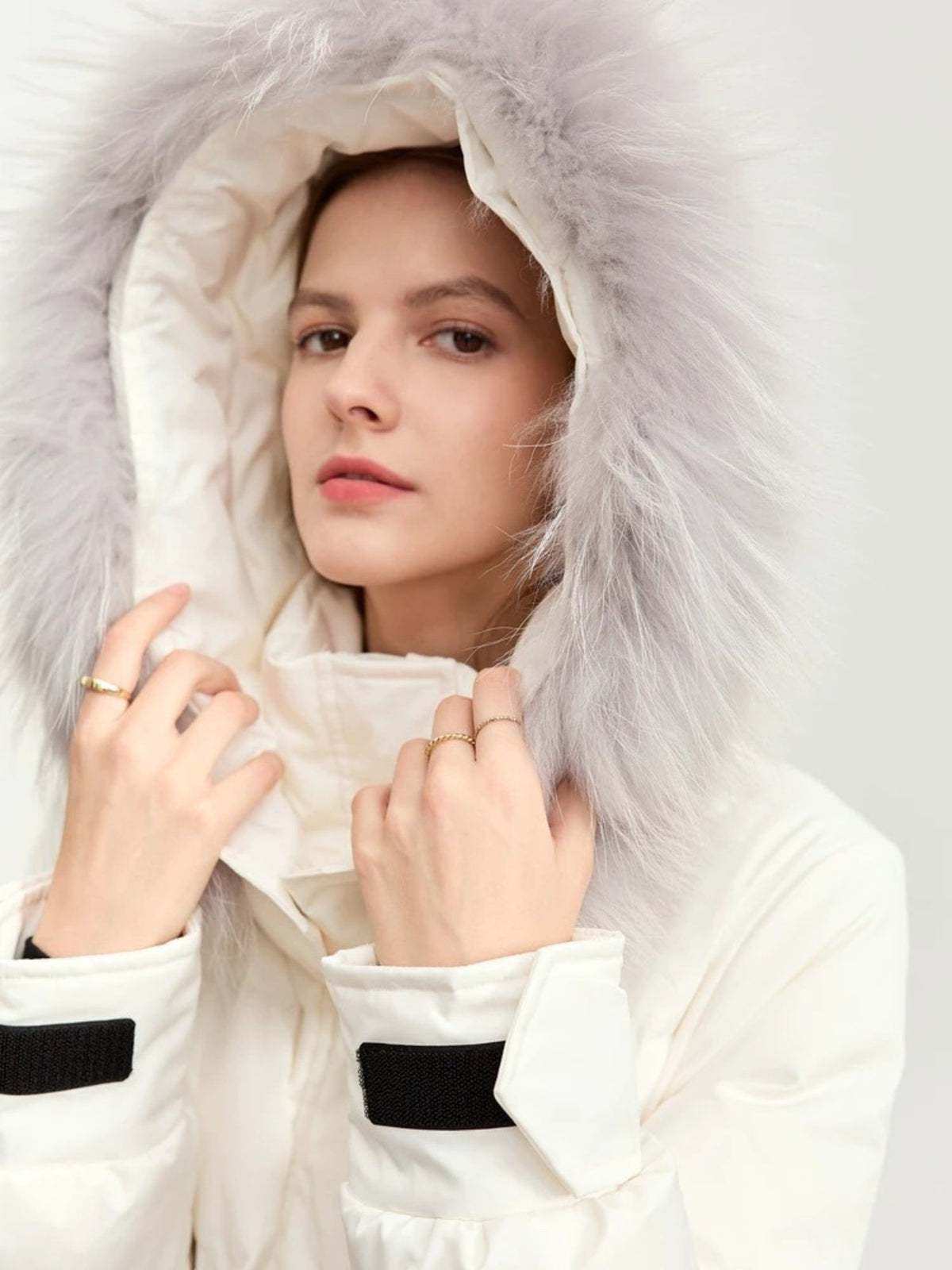 Model with hood up wearing white puffer coat, hands adjusting collar