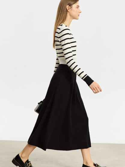 Woman wearing a black and white striped sweater and black skirt on a plain background